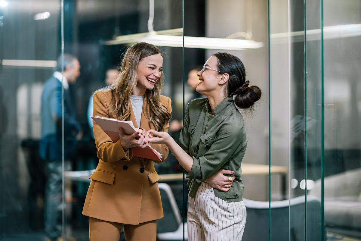 AdobeStock_1260914106 Smiling colleagues discussing IT and HR access tracking in a modern office environment.