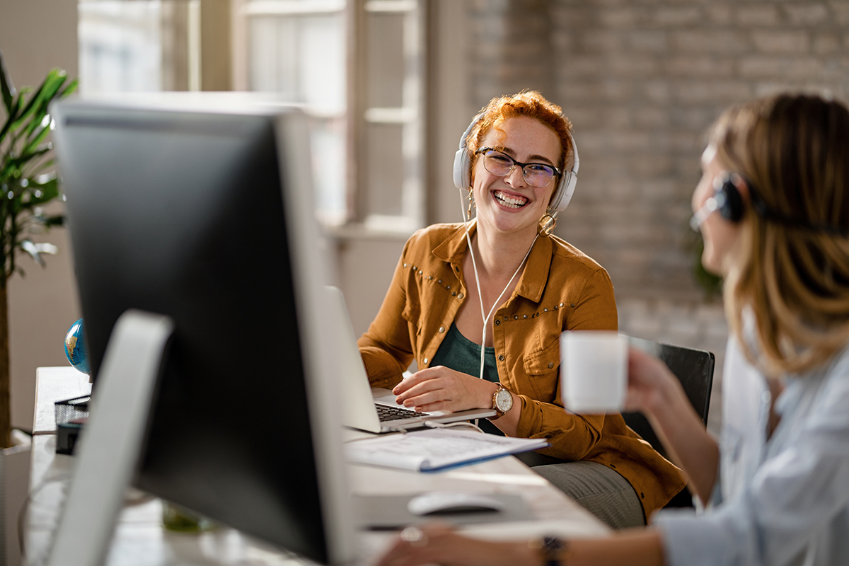 Happy businesswoman talking to her colleague while working on laptop in the office. Employée utilisant un logiciel d’automatisation C2 ITSM pour gérer les tâches répétitives
