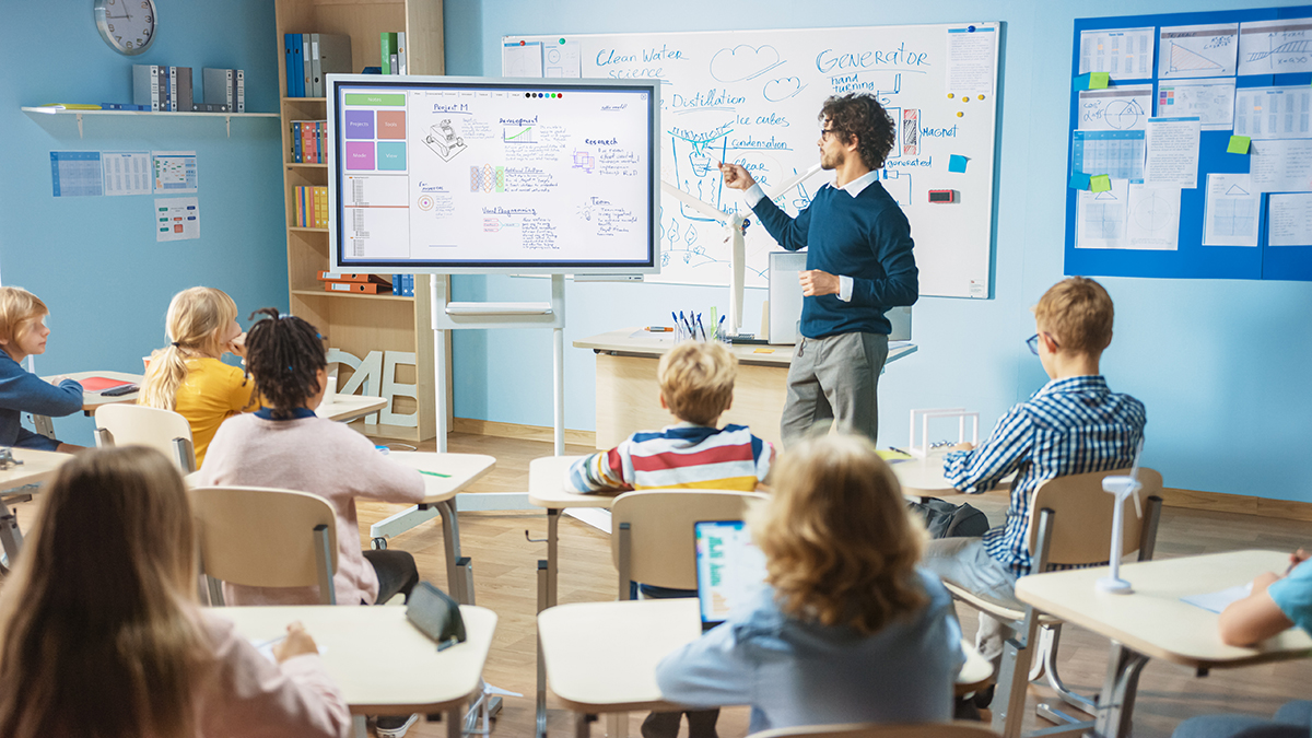 Elementary School Science Teacher Uses Interactive Digital White Teacher presenting on an interactive whiteboard in a modern classroom, representing streamlined IT management for education with C2 ITSM.
