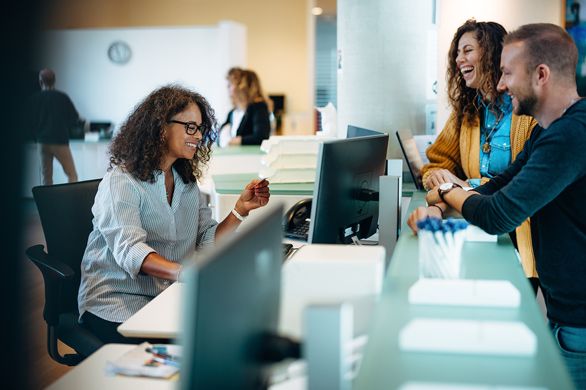Receptionist assisting people standing at front desk Équipe TI collaborant sur des projets stratégiques grâce à l’automatisation des tâches avec C2 ITSM