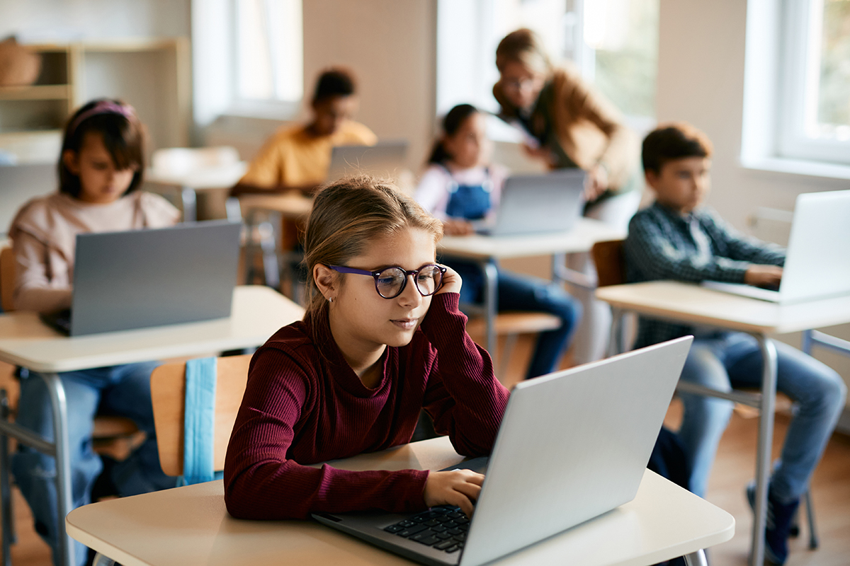 Little girl e-learns on laptop in computer science classroom at elementary school. Students using laptops in a classroom, representing effective management of digital and educational resources.