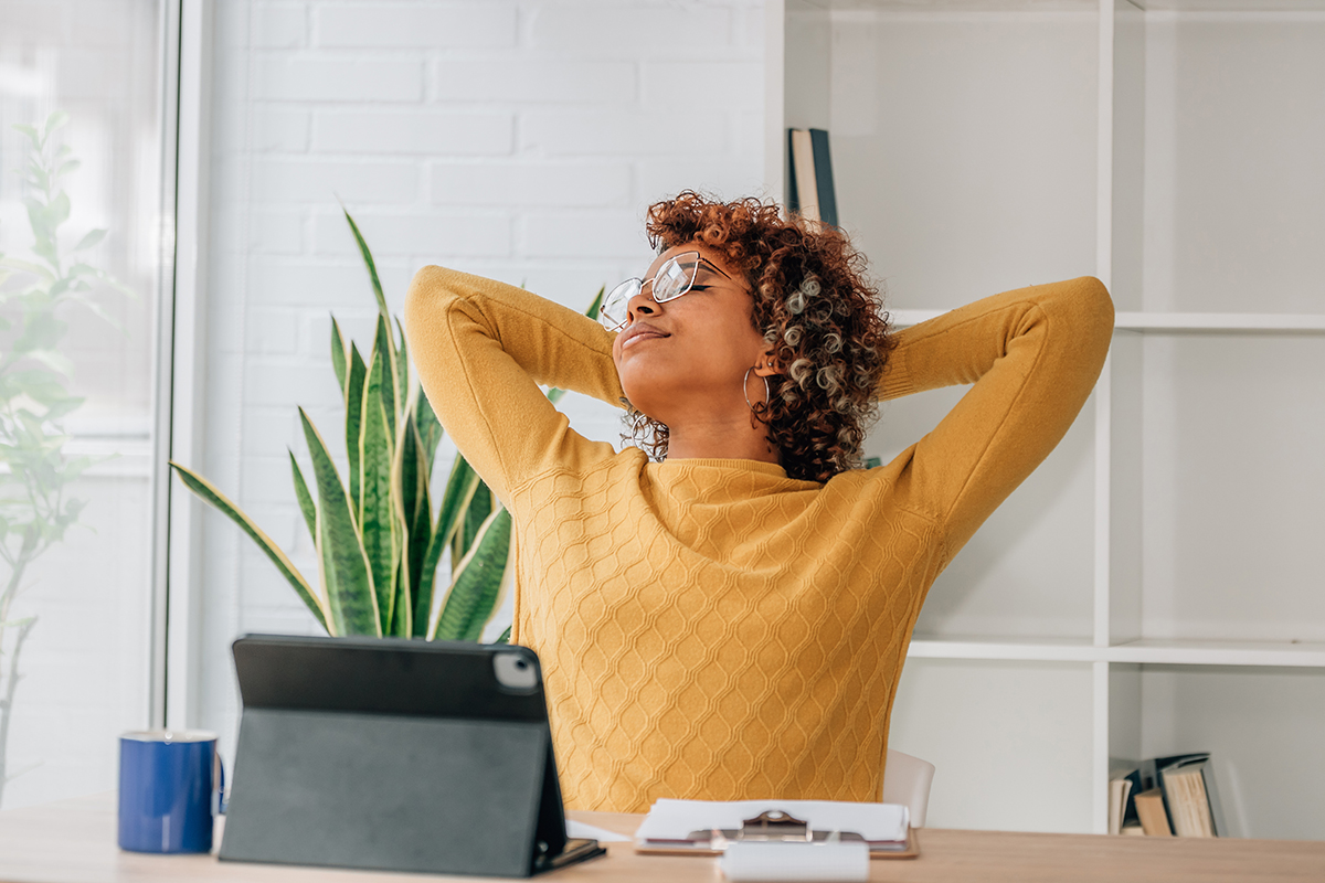 african american woman with laptop relaxing at home Smiling woman stretching at her desk, relaxed after completing tasks, symbolizing improved IT service quality