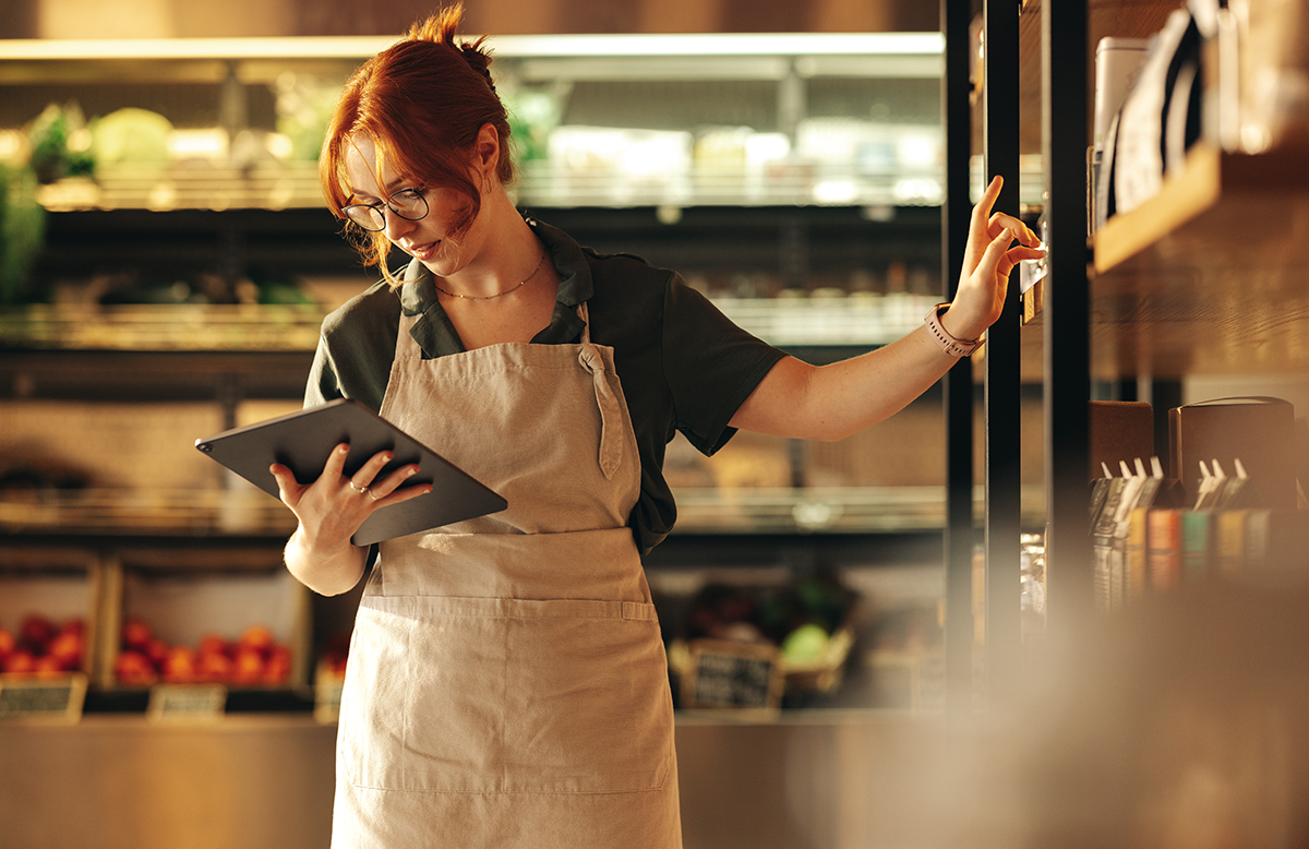 Supermarket owner using a digital tablet in her shop Employee managing inventory with a digital tablet, representing centralized asset and inventory management in C2