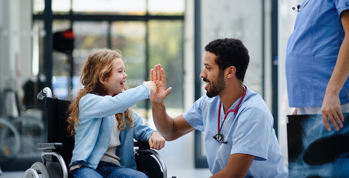AdobeStock_553231584 A smiling healthcare worker high-fives a young patient in a wheelchair, symbolizing collaboration and responsive care supported by C2 ITSM.