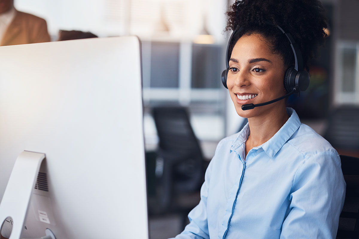 AdobeStock_575246813 Administrative professional with a headset smiling at her desk – centralized request management through C2